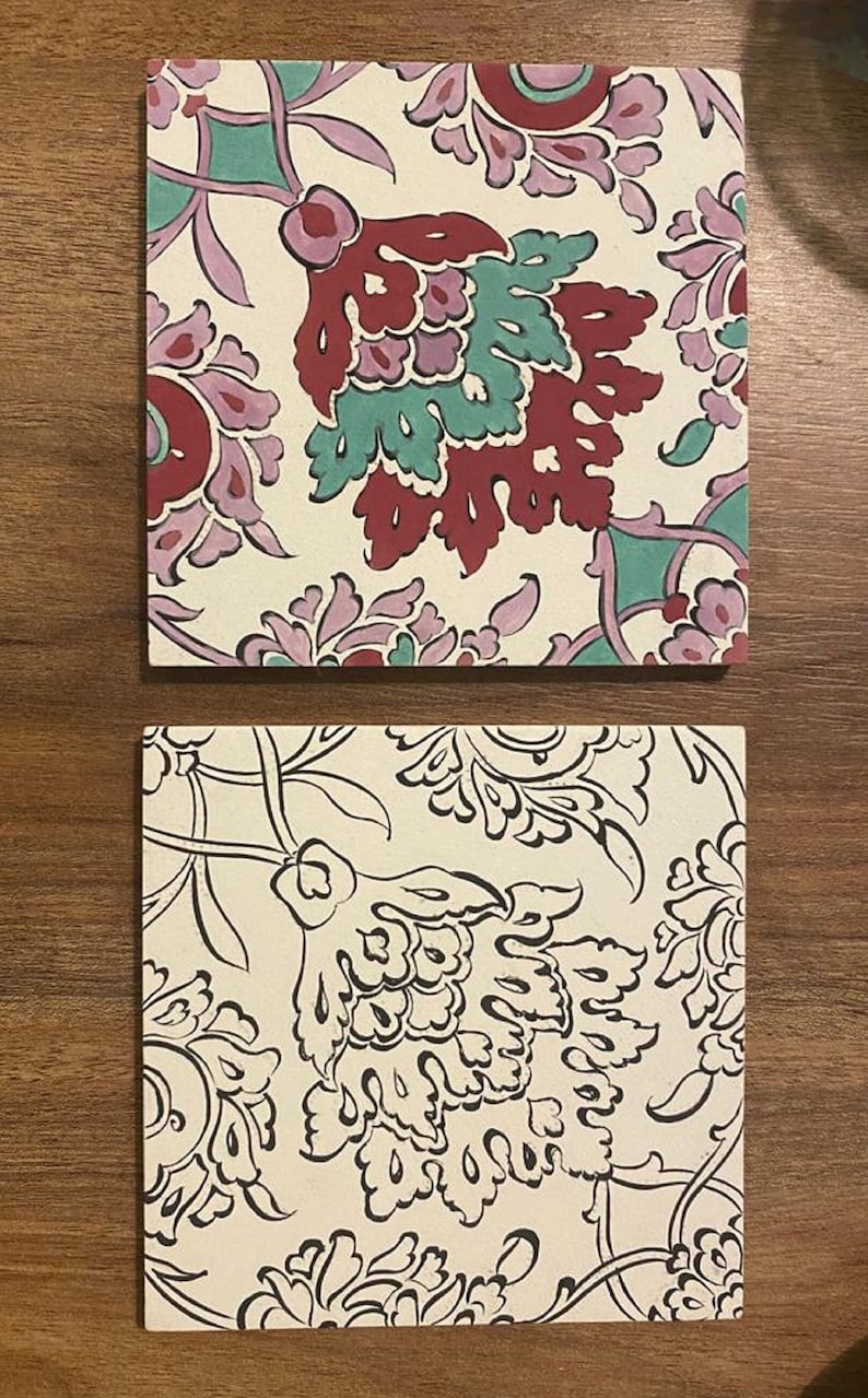 May include: Two square ceramic tiles with a white background and floral patterns. The top tile has a red, pink, and green floral pattern. The bottom tile has a black floral pattern.