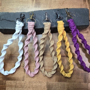 May include: Six colorful, twisted, rope keychains with metal clasps. The keychains are white, pink, beige, yellow, and purple.