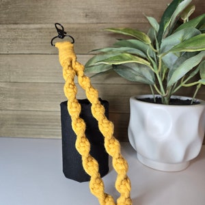 May include: A yellow braided keychain with a black metal clasp. The keychain is hanging from a black fabric tube.