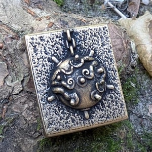 May include: A square-shaped pendant with a detailed, ornate design of a ladybug. The pendant is made of a metallic material with a textured surface and is hanging from a chain.