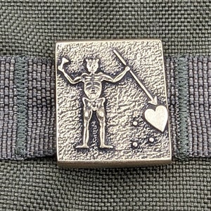 以下が含まれることがあります： 緑色の布地に、槍とハートを持った骸骨が描かれた金色の金属製のピン。