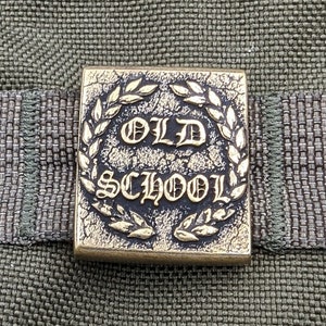 May include: A gold-colored metal square patch with a laurel wreath design and the words "OLD SCHOOL" in a stylized font.
