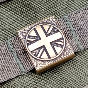 Peut inclure: Un charme carré en laiton avec un motif circulaire en relief du drapeau britannique.