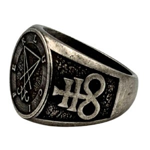 May include: A silver-toned metal ring with a weathered finish. The circular face features a sigil of Lucifer with the letters L, U, C, I, F, E, R arranged around the border. The side of the band displays a raised Leviathan cross symbol.
