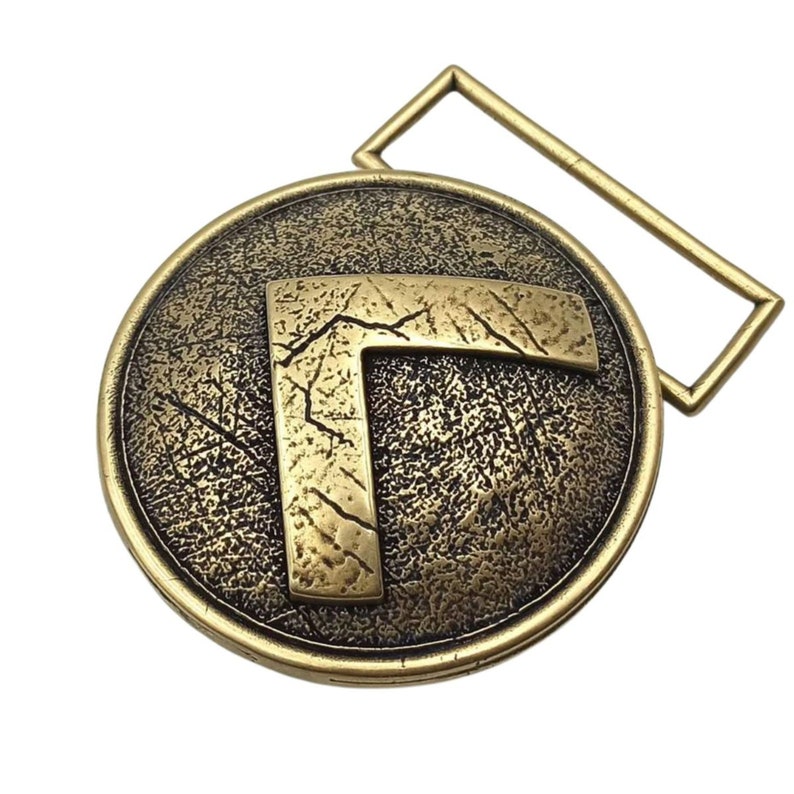 May include: A circular brass belt buckle with an antique finish featuring a raised, weathered letter L in the centre. The background of the circle has a textured, cracked appearance, and the buckle includes a rectangular loop for attachment.