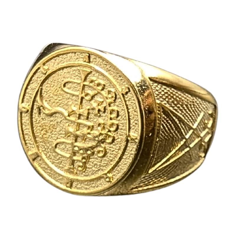 May include: A gold ring with a circular design featuring a snake wrapped around a staff with wings. The ring has a textured band.