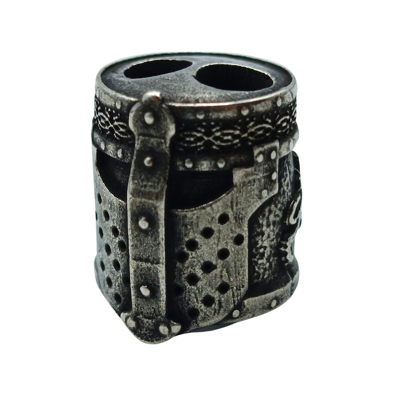 May include: A silver metal bead with a detailed design of a knight's helmet. The bead has a textured surface and a raised design.
