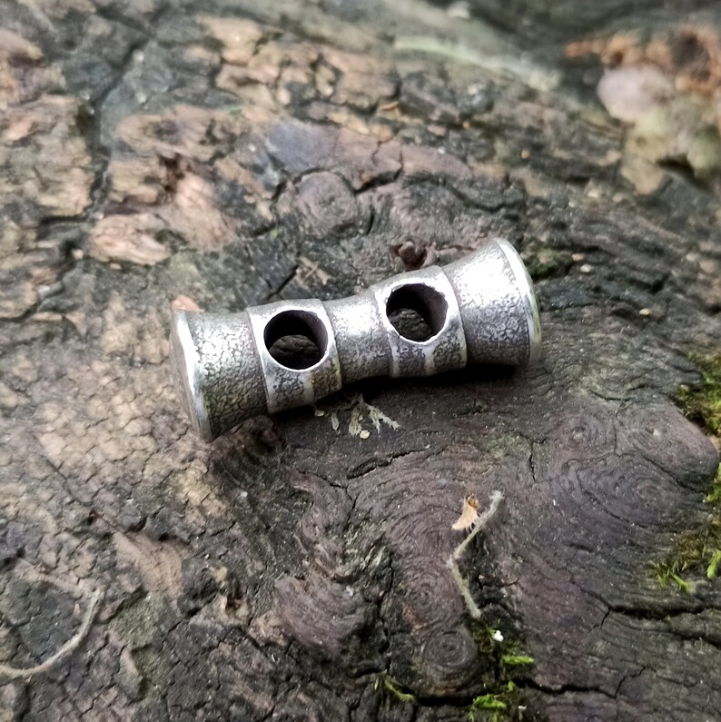 May include: A silver metal toggle with two holes, designed for use in clothing or accessories.
