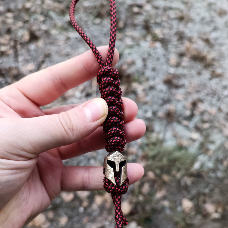 May include: A black and red paracord keychain with a bronze Spartan helmet charm.