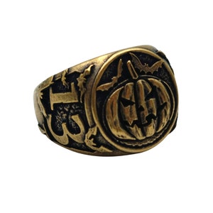Puede incluir: Un anillo de tono dorado con un dise&ntilde;o detallado de una calabaza de Halloween con murci&eacute;lagos volando a su alrededor. El anillo est&aacute; grabado con la palabra "1313".