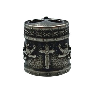 May include: A silver metal bead with a cross and two winged figures on the front. The bead has a textured surface and a decorative band around the top.