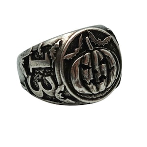 Puede incluir: Un anillo de plata con un dise&ntilde;o detallado que presenta una calabaza con una cara tallada, murci&eacute;lagos y otros elementos espeluznantes.