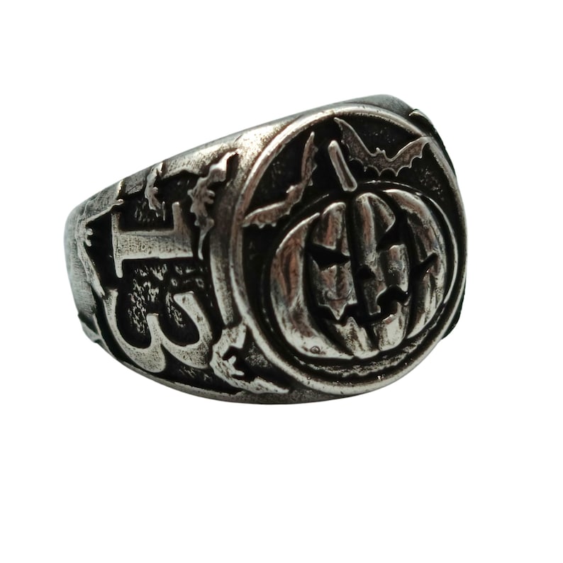 Puede incluir: Un anillo de plata con un dise&ntilde;o detallado que presenta una calabaza con una cara tallada, murci&eacute;lagos y otros elementos espeluznantes.