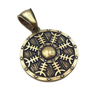 May include: A round, gold-toned pendant in the shape of a shield with a stylised sun symbol in the centre. The shield has a textured surface and a beaded edge.