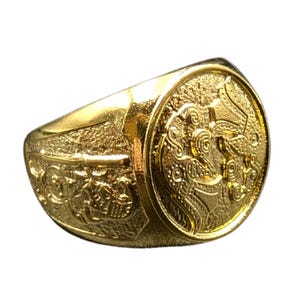 May include: A gold ring with an intricate design featuring a mythical creature. The ring has a wide band and a large, round face.