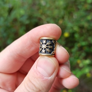 May include: A gold and black metal bead with a Vegvisir symbol engraved on it.