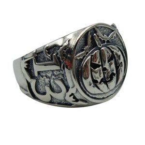 Puede incluir: Un anillo de plata con un dise&ntilde;o detallado que presenta una calabaza con una cara tallada y el n&uacute;mero "13" en el lateral.