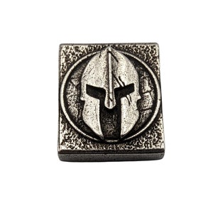 May include: A silver-toned metal square charm with a raised image of a Spartan helmet in a circle.