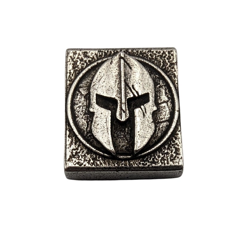 May include: A silver-toned metal square charm with a raised image of a Spartan helmet in a circle.