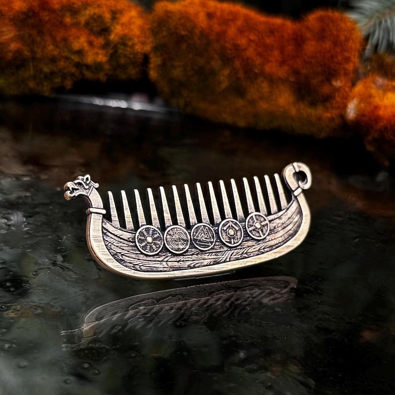 Bronze beard comb Viking ship Drakkar comb with intricate detailing. The comb features a dragon head at the front and a curved design at the back. Shields with various symbols are etched along the ship's side. The comb's teeth are evenly spaced.