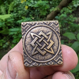 Op de afbeelding: Een bronzen hanger met een geometrisch sterontwerp. De ster is gemaakt van verweven lijnen en is omgeven door een decoratieve rand.