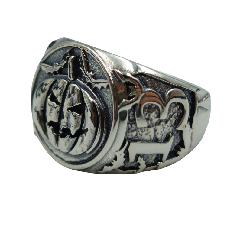 Puede incluir: Un anillo de plata con una talla detallada de una calabaza de Halloween en un lado y el n&uacute;mero "13" en el otro.