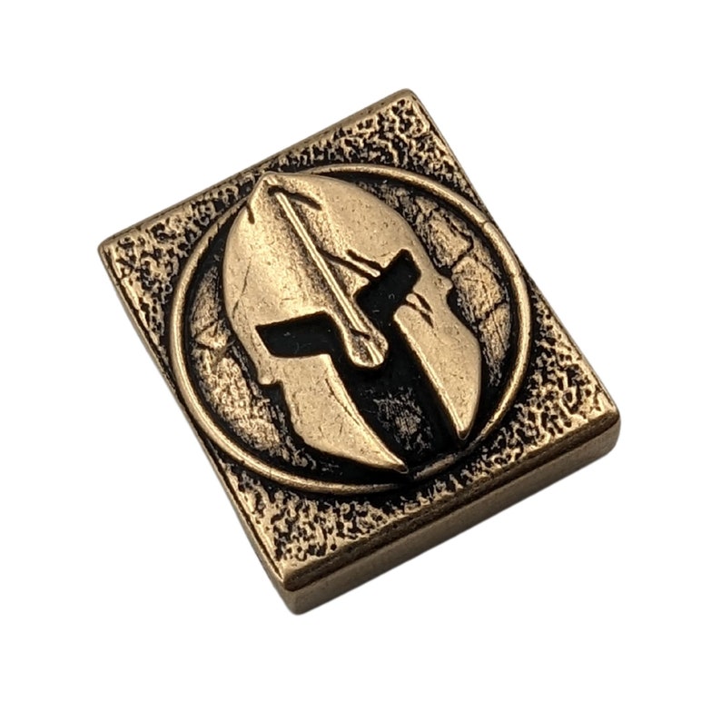 May include: A gold-colored metal square charm with a raised, black and gold Spartan helmet design.