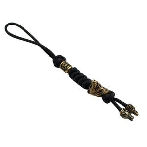 May include: Black paracord keychain with a gold metal bead and two wolf head charms.