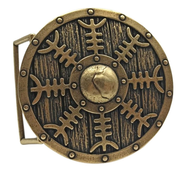 May include: A gold-toned belt buckle with a round design. The buckle features a circular shield with a wood grain texture and a central boss. The shield is decorated with a repeating pattern of stylised branches.