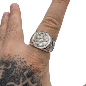 A silver ring with a circular design featuring a Azazel sigil. The ring has a textured band.