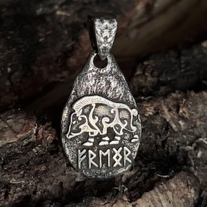 May include: A teardrop-shaped metal pendant with a dark, weathered finish. The surface features a raised relief of a stylized boar in profile, positioned above a row of five engraved runic characters. A sturdy bail is attached at the top.