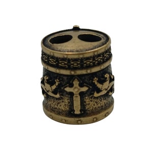 May include: A gold-toned metal bead with a cross design and two holes. The bead has a textured surface and a decorative band around the top.