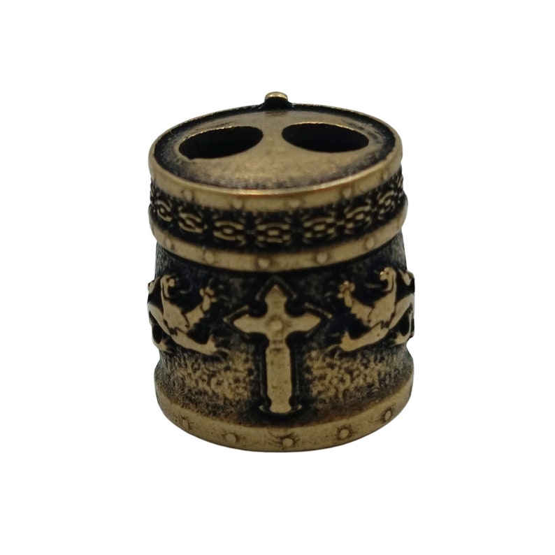 May include: A gold-toned metal bead with a cross design and two holes. The bead has a textured surface and a decorative band around the top.