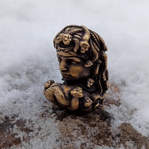 Puede incluir: Una escultura de bronce de una mujer con serpientes en el pelo. La escultura es detallada e intrincada, con el rostro y el cabello de la mujer claramente visibles. Las serpientes est&aacute;n enroscadas alrededor de su cabeza y cuello, y sus escamas son visibles.