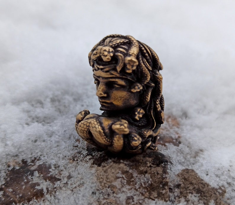 Puede incluir: Una escultura de bronce de una mujer con serpientes en el pelo. La escultura es detallada e intrincada, con el rostro y el cabello de la mujer claramente visibles. Las serpientes est&aacute;n enroscadas alrededor de su cabeza y cuello, y sus escamas son visibles.