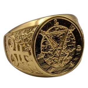May include: A gold-toned ring featuring a textured surface with a central circular emblem displaying the Sigil of Lucifer. The letters L, U, C, and I are embossed around the perimeter of the circle, and a symbol is engraved on the side of the band.