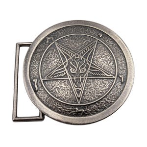 May include: A round, silver-toned metal belt buckle with a textured, antiqued finish. The center features an embossed pentagram design containing a stylized goat head. Hebrew characters are engraved along the circular border of the buckle.