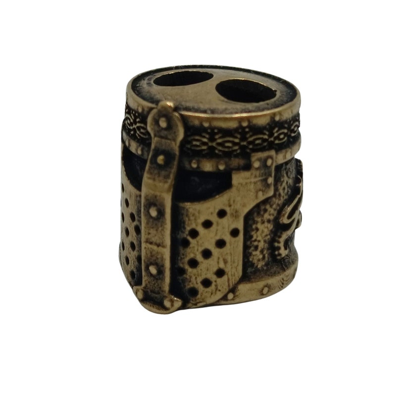 May include: A bronze-colored metal bead with a detailed design of a knight's helmet. The bead has two holes for threading.