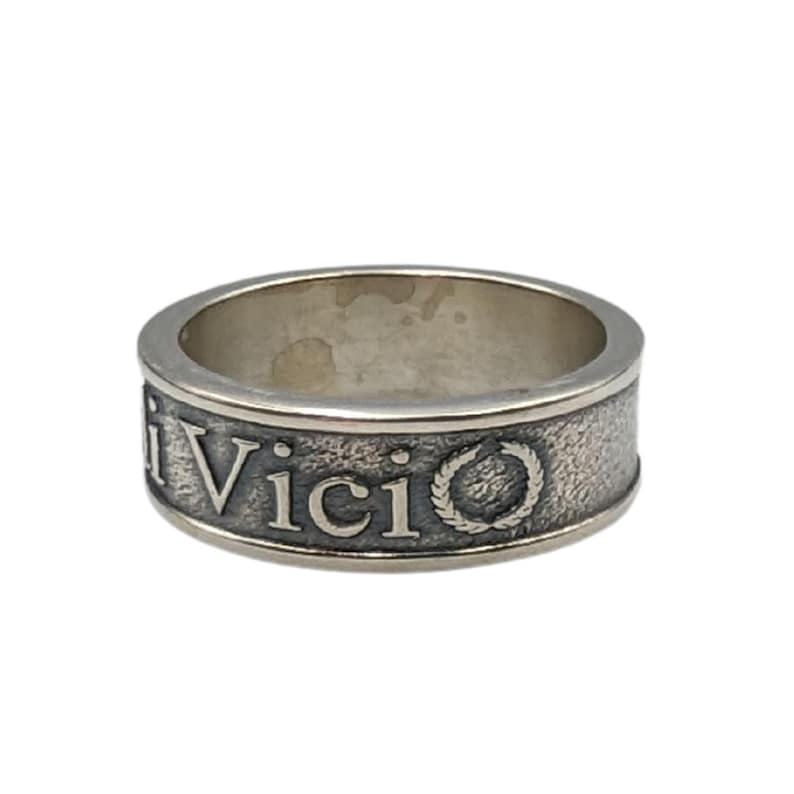 May include: A silver-toned metal ring with a textured, oxidised finish. The band features the embossed text "Vici" followed by a circular laurel wreath emblem. The interior of the band is smooth and polished, contrasting with the dark, rugged exterior surface.