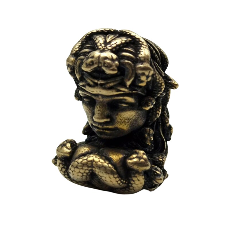 Puede incluir: Una escultura de metal dorado de Medusa, la figura mitol&oacute;gica griega con serpientes por cabello. La escultura est&aacute; detallada con serpientes envueltas alrededor de su cabeza y cuello.