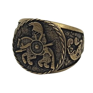May include: A bronze ring with a detailed design of a warrior on horseback. The ring has a textured band and a circular design on the top.