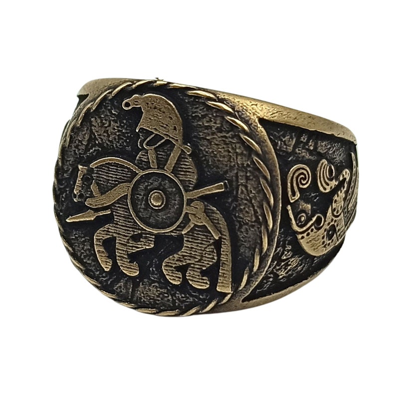 May include: A bronze ring with a detailed design of a warrior on horseback. The ring has a textured band and a circular design on the top.