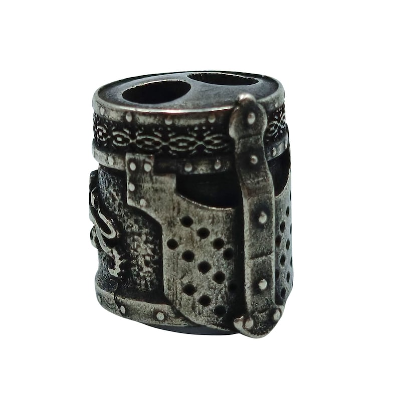 May include: A silver metal charm in the shape of a knight's helmet. The helmet has a detailed design with a visor and a chainmail pattern.