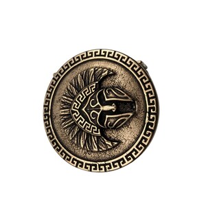 May include: A circular bronze-toned belt buckle featuring a central embossed Spartan helmet design. The outer edge is decorated with a repeating Greek key pattern. The metal surface has a weathered, antiqued finish with dark recessed details.