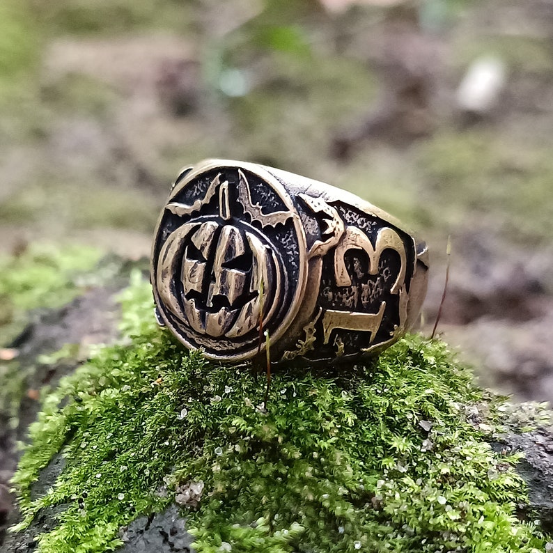 Puede incluir: Un anillo de bronce con una calabaza tallada y el n&uacute;mero 13. El anillo est&aacute; sobre un lecho de musgo verde.