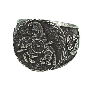May include: A silver ring with a detailed design of a warrior on horseback. The ring has a rope-like border and a stylized wave design on the side.