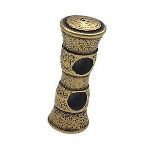 May include: A gold-coloured metal bead with two circular holes. The bead has a textured surface and a rounded top.