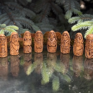 May include: A set of ten small, hand-carved wooden figurines arranged in a row. Each figure features distinct facial expressions, detailed clothing, and carved patterns, with a light brown wood grain finish and a smooth, polished appearance.
