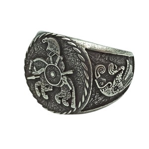 May include: A silver ring with a detailed design of a warrior riding a chariot pulled by two horses. The ring has a textured surface and a rope-like border.