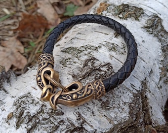May include: A black leather bracelet with a bronze clasp featuring a detailed Viking knot design.